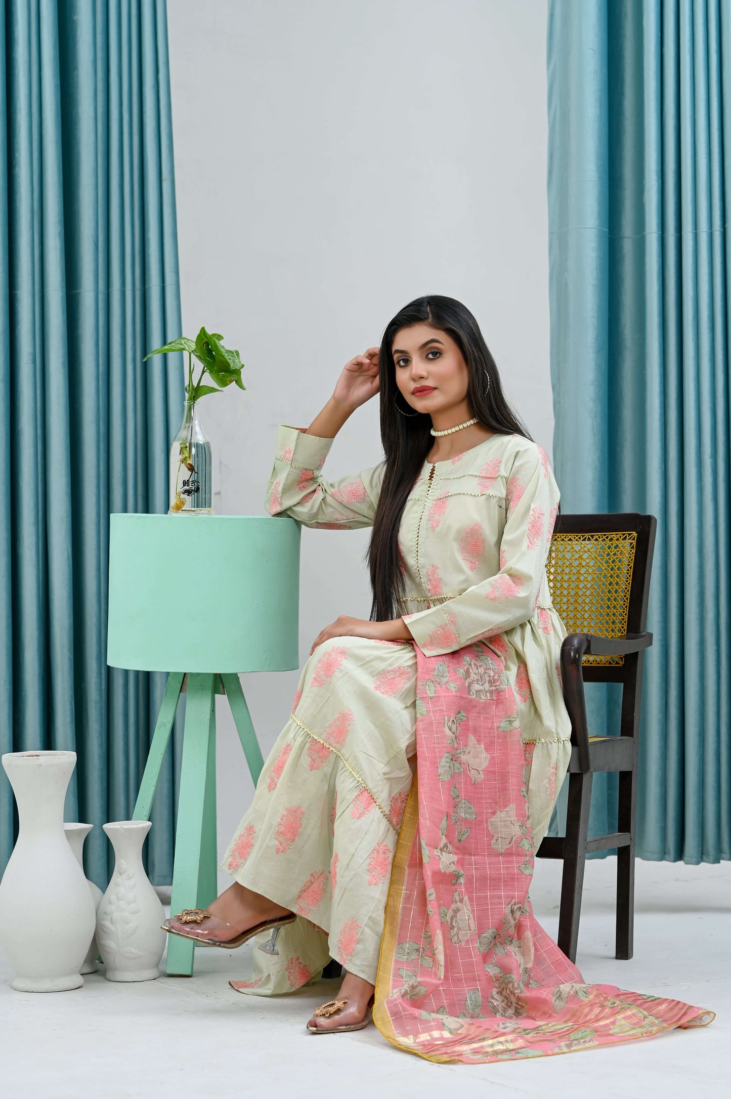 Model wearing a 2-piece light green frock with a pink dupatta, seated gracefully in a minimalist setting.